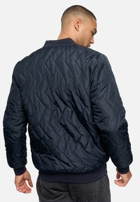 Chaqueta bomber acolchada en color navy con un patrón de chevron texturizado y puños y dobladillo de canalé, que cuenta con un cuello clásico y cierre de cremallera.