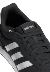 Baskets noires avec tige en synthétique, présentant trois bandes blanches, un système de laçage et un col rembourré. Semelle extérieure en caoutchouc avec grip texturé.