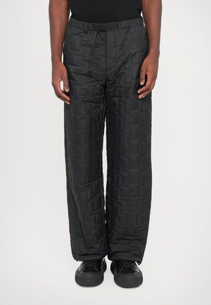 Black quilted pants with a relaxed fit, featuring a drawstring waistband and geometric patterns, paired with black shoes.