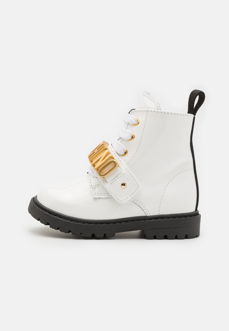Bottines en cuir verni blanc avec accent de sangle dorée, lacets blancs, semelle noire et semelle texturée. Comprend une languette à l'arrière pour un enfilage facile.
