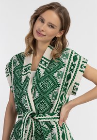 Kimono verde e crema con motivo a fantasia, maniche corte, caratteristiche geometrie e vita regolabile con cintura. Tessuto morbido.
