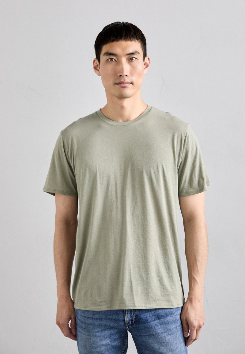 T-shirt vert clair à manches courtes en tissu doux avec un col rond, associé à un jean bleu, porté par un modèle masculin.