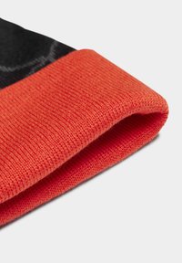 Tessuto a maglia rosso con una finitura textured, caratterizzato da un bordo piegato. Un tessuto di colore più scuro è visibile sopra la piega, creando un contrasto.