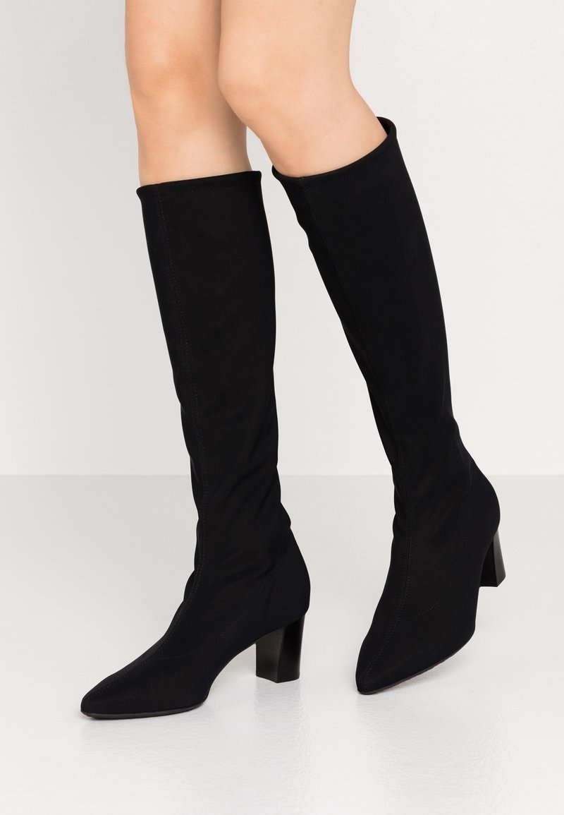 Bottes noires montantes en tissu doux, avec un bout pointu et un talon épais, présentant une texture lisse et un design sans couture.
