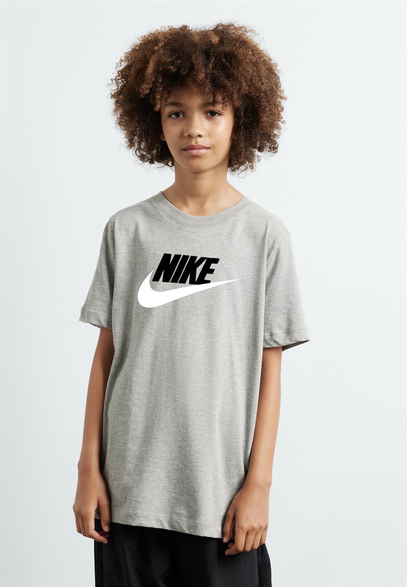 Pilka trumpa rankovė t-shirt, pagaminta iš minkštos medžiagos, su dideliu juodu Nike logotipu ant krūtinės ir baltu swoosh akcentu.