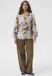 Hosszú ujjú blúz kék, bézs és barna absztrakt mintával, V-nyakkivágással és rugalmas mandzsettákkal, barna, bő szárú nadrággal párosítva.