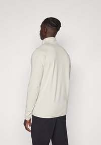 Maglione in pile beige chiaro con zip, collo alto, texture a coste e maniche lunghe, abbinato a pantaloni scuri.