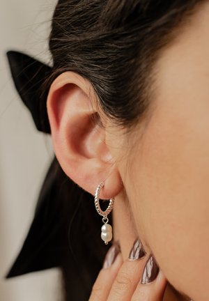 Silver hoop earring with a twisted design featuring a dangling white pearl. Close-up view highlighting texture and detail against skin.