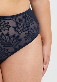 Culotte taille haute bleu marine avec des détails en dentelle florale, en tissu lisse et avec une ceinture contrastée. Accentuée par un motif texturé.