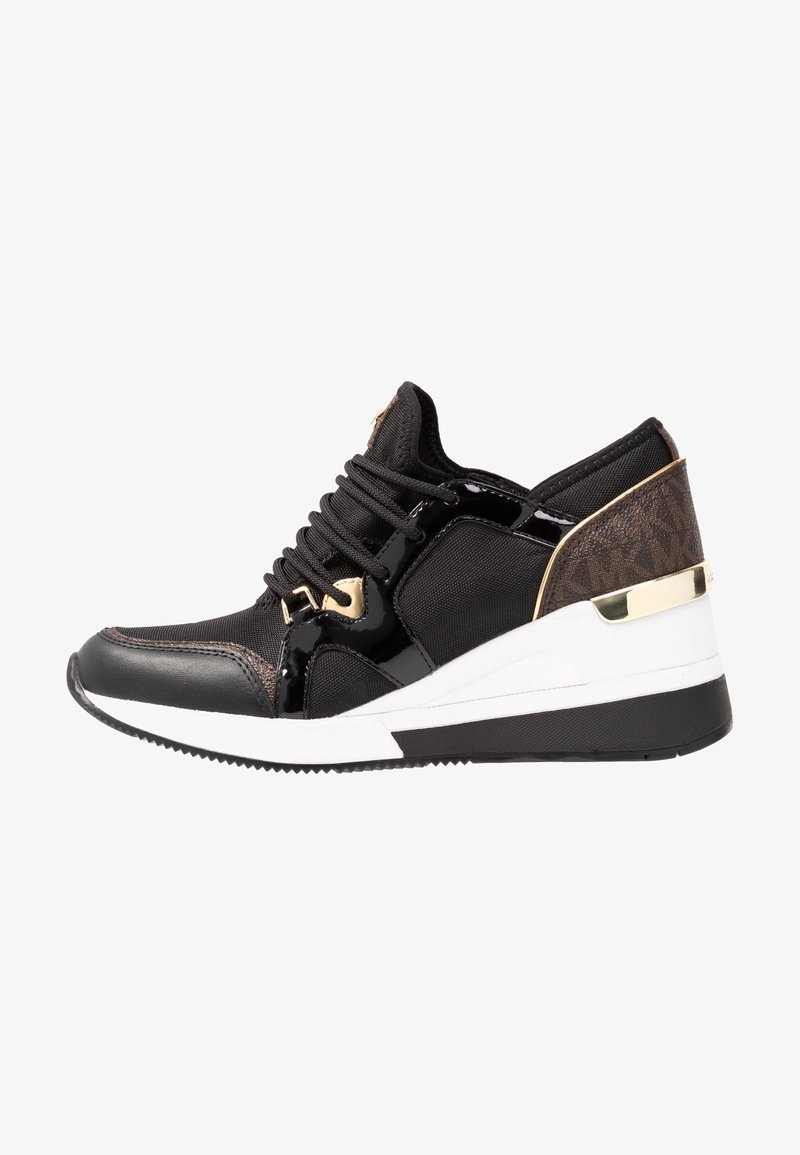 Black sneaker features a textured fabric upper with patent leather accents, gold hardware, and a white midsole with a contrasting black outsole.