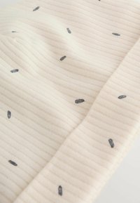 Tissu côtelé crème avec de petits points ovales noirs uniformément espacés répartis sur toute la surface.