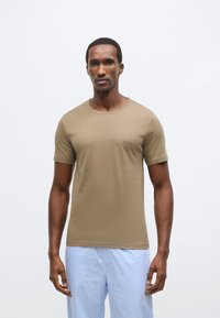 Kaki majica s kratkimi rokavi, okroglim izrezom in diskretno podrobnostjo logotipa. Mehka tekstura, prilegajoč se kroj, v kombinaciji s svetlo modrimi hlačami s karirastim vzorcem.