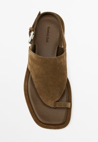 Sandale en daim marron avec une bride arrière, design ouvert à l'avant, forme carrée et semelle intérieure marron foncé. Présente un détail de boucle en métal.