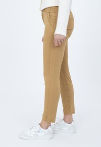 Vaqueros skinny color beige con una textura suave, con detalles de costura y una cintura de altura media, combinados con zapatillas blancas para un look casual.