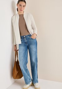 Světlounce šedá texturovaná bunda přes hnědý top, doplněná volnými modrými džíny. Hnědá semišová kabelka přes rameno a bílé tenisky s modrými akcenty.