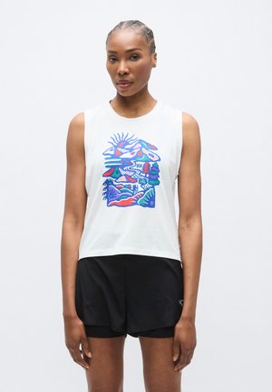 Άσπρο αμάνικο τοπ cropped με πολύχρωμο γραφικό σχέδιο από βουνά και δέντρα. Μαύρο σορτσάκι με στρωματοποιημένη εμφάνιση ολοκληρώνει το σύνολο.