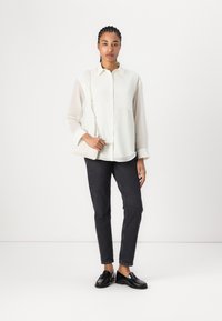 Hvit langermet skjorte med knappelukking og lomme, parret med mørke jeans og svarte loafers, holder en strukturert hvit veske.