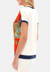 T-shirt z krótkim rękawem w odważny czerwono-niebieski wzór, z białym korpusem i granatowym wykończeniem przy kołnierzyku i dolnej krawędzi, wykonany z gładkiego materiału.