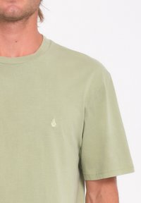 Camiseta de algodón verde claro con mangas cortas y cuello redondo. Presenta un pequeño logo blanco en el área del lado izquierdo del pecho.