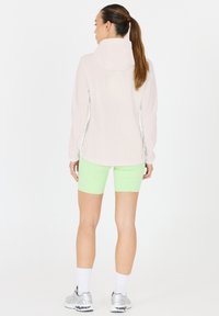 Lätviktsvit jacka med huva, i kombination med neongröna shorts. Shortsen har en mjuk yta och outfiten fulländas med silversneakers.