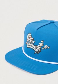 Zils beisbola cepure ar multfilmu tēlu, kas attēlo dūmojošu dzīvnieku galvu, kas valkā baltu cepuri ar sarkanu svītru un uzrakstu "Ralbm".