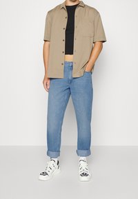 Tan krátký rukávový svetr přes černýcrop top, spárovaný s ohrnutými modrými džíny a bílými teniskami s černými akcenty.