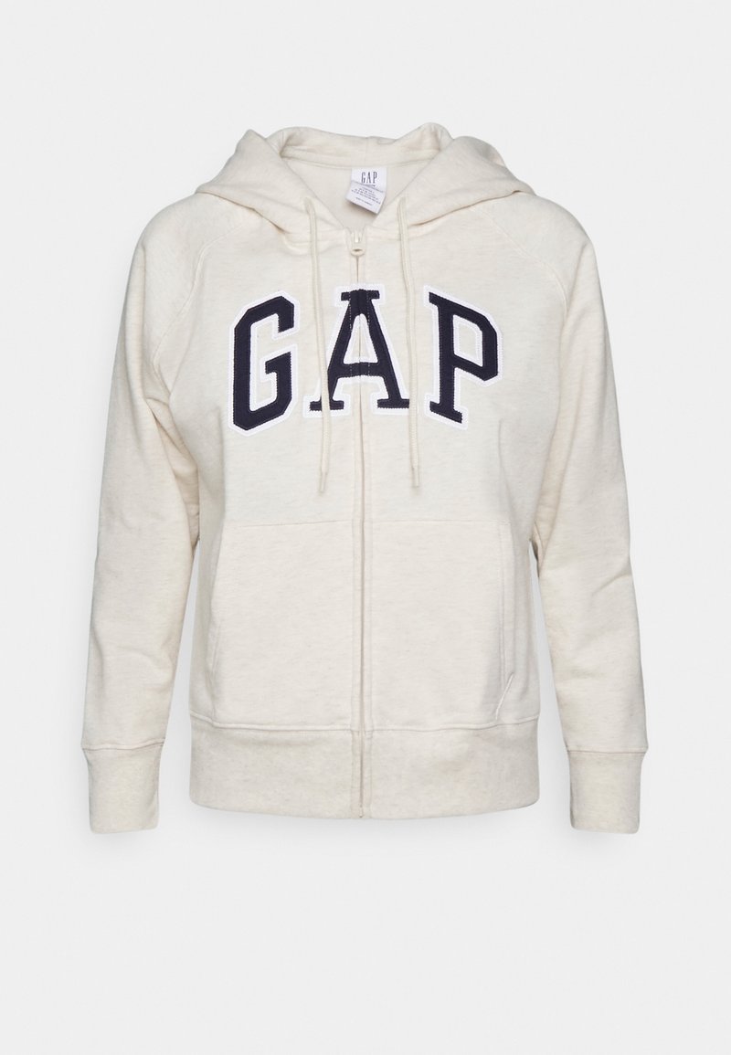 Sweat à capuche crème à fermeture éclair avec capuche à cordon, arborant un grand logo "GAP" bleu marine. Matière douce, poches avant et poignets côtelés.