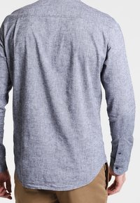 Långärmad skjorta i ljusblått texturerat tyg, med knappförsedda manschetter och rundad fåll. Bakvyn visar en enkel design utan mönster.