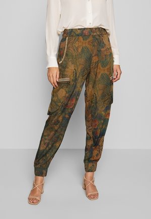 Mujer con pantalones cargo estampados de talle alto y bolsillos con cordón, combinados con una blusa blanca y sandalias de tacón beige.