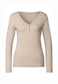 Haut beige à manches longues avec un décolleté en V, patte de boutonnage à deux boutons et silhouette ajustée. Fabriqué en tissu doux et lisse avec un design simple.