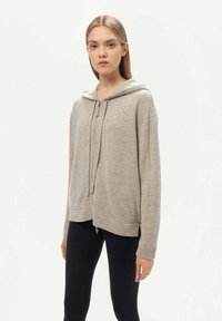 Huvtröja i ljusgrått stickat material med dragsko i huvan. Har en avslappnad passform, långa ärmar samt ribbad nederkant och ärmslut.