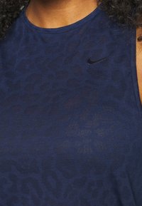 Mörkblå ärmlös topp gjord av mjukt tyg med ett subtilt leopardmönster, med en liten svart Nike-logotyp på vänster bröstområde.