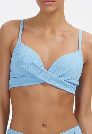 Kobieta w teksturowanym, jasnoniebieskim staniku bikini z cienkimi ramiączkami i krzyżującym się wzorem z przodu, odsłaniającym brzuch, na neutralnym tle.