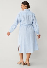 Lyseblå stribede skjortekjole med lange ærmer, indsnøret talje, sideslids og krave. Bæres med beige blokhælede sandaler.