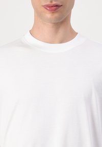 Effen wit katoenen T-shirt met een geribde kraag. Zachte textuur, losse pasvorm, minimalistisch ontwerp, geen zichtbare patronen of accenten.