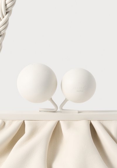 Λευκή τσάντα με υφασμένη, ριγέ βάση από δέρμα· διαθέτει δύο στρογγυλές λευκές σφαίρες που συνδέονται με καμπύλες λευκές υποστηρίξεις. Μινιμαλιστικός σχεδιασμός.