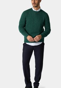 Zelený pletený svetr s texturovaným povrchem, kulatým výstřihem a žebrovaným lemem. V kombinaci s námořnickými kalhotami a bílou košilí s límečkem pod ním.