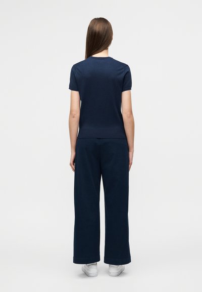 Μπλε ναυτικό μπλουζάκι και παντελόνι με φαρδιά μπάσκα από απαλό ύφασμα. Απλός σχεδιασμός με στρογγυλή λαιμόκοψη και κοντά μανίκια. Λευκά παπούτσια.