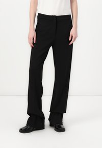 Pantaloni neri a gamba larga realizzati in tessuto morbido, con chiusura a bottone, leggere pieghe frontali e una vestibilità rilassata in fondo.