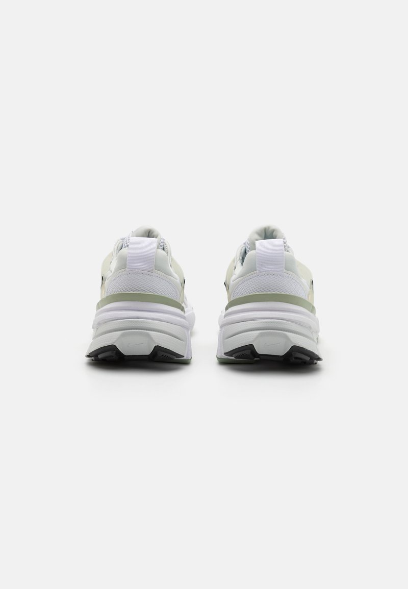 Des chaussures de sport blanches avec une tige texturée, un collier rembourré et une forme de semelle distincte ; avec des accents verts et un logo visible à l'arrière.