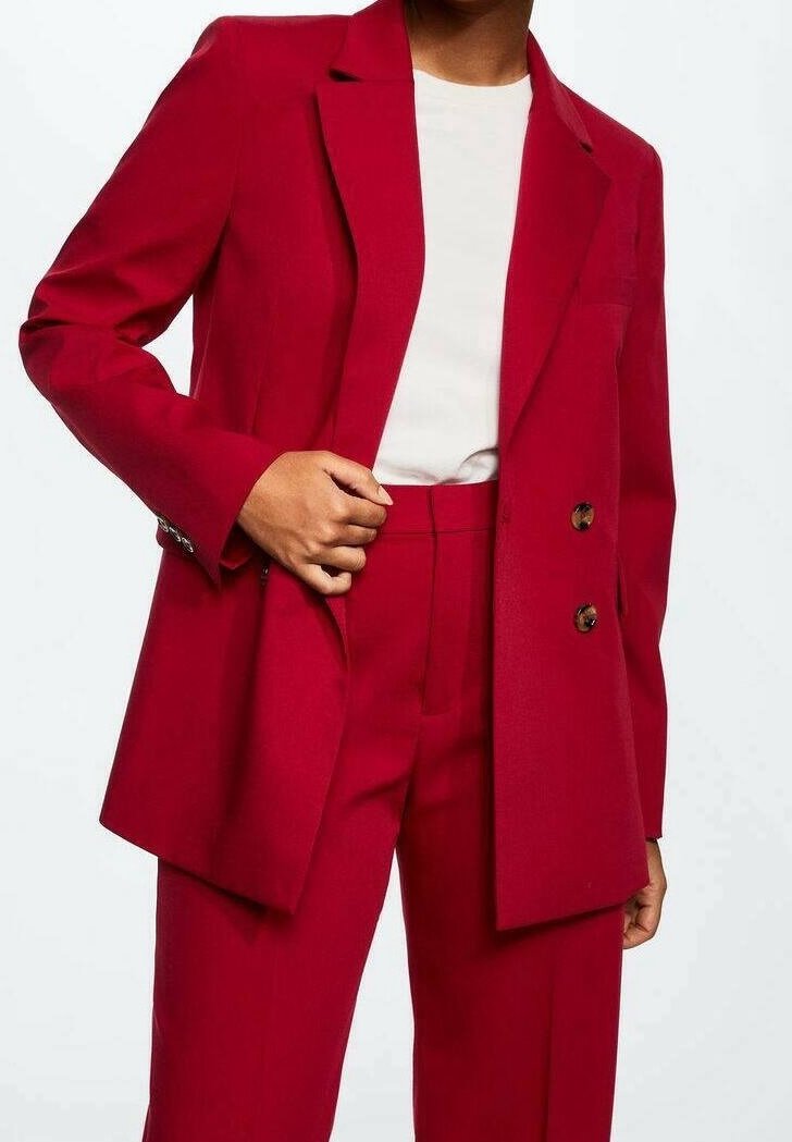 Červený blazer a odpovídající kalhoty vyrobené z hladké tkaniny. Blazer má dvouřadý design a klopové límce.