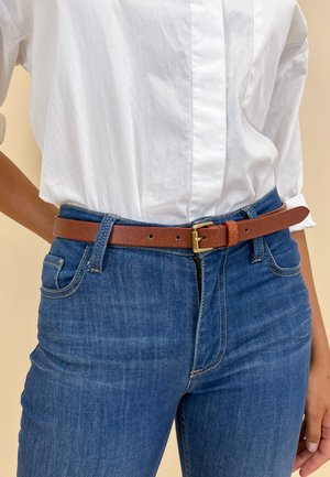 Brown leather belt with a gold buckle, worn over blue denim jeans, paired with a white collared shirt. Smooth texture, simple design.