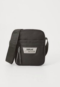 Czarna torebka na ramię z tkaniny o prostokątnym kształcie, wyposażona w przednią kieszeń na zamek, naszywkę z logo oraz pleciony pasek z tekstowym detalem.