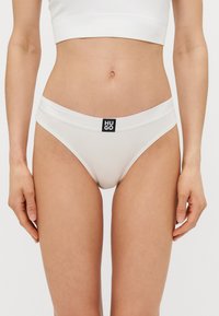 Culotte de bikini blanche à côtes avec une large ceinture et une étiquette noire Hugo à l'avant. Le matériau semble lisse, avec un design ajusté.