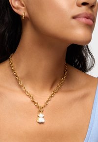 Collier en chaîne en or avec de grands maillons et un pendentif en forme d'ours blanc, présentant une texture douce. Le design simple met l'accent sur des éléments ludiques.