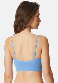 Reggiseno blu chiaro con spalline regolabili, una texture liscia e un design semplice. La vista posteriore mette in evidenza il materiale elasticizzato e una finitura senza cuciture.