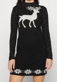 Svartstickad klänning med en vit ren-design, pärlprydnader på ärmarna och ett vitt snöflingemönster längs fållen.