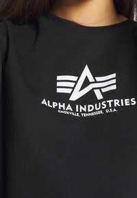 Gros plan sur une chemise noire avec un logo Alpha Industries blanc et le texte « Knoxville, Tennessee, États-Unis » sur la poitrine.