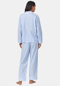 Gestreept blauw pyjama set met een lange mouw overhemd met knopen en bijpassende broek. Zachte stof, losse pasvorm, opgerolde manchetten en zijzakken.