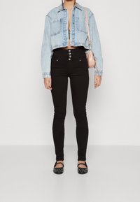Chaqueta de mezclilla azul claro, cortada, con cierre de botones, combinada con jeans skinny negros de cintura alta con cinco botones y zapatos planos negros con tachuelas.